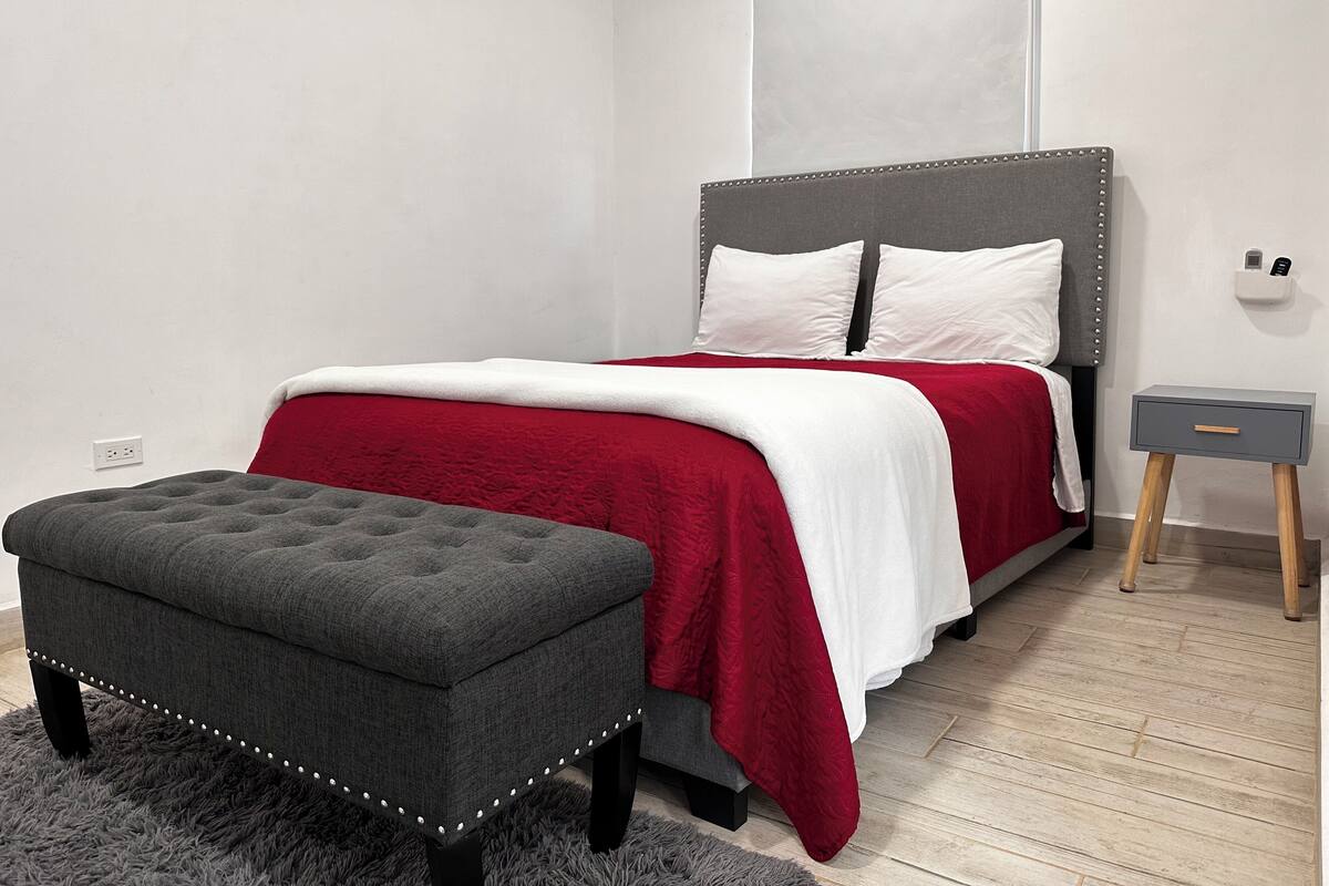 A bedroom with a bed, bedside table, and a small ottoman.
