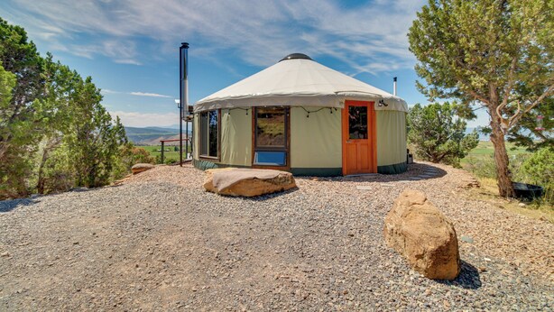 Una yurta con una porta rossa, circondata da alberi e un vialetto sterrato.