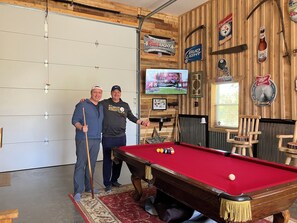 A pool table in a room with wooden walls, a television displaying a sports event, and various beer brand memorabilia. - Bull Run Lodge Unique 2000 sq. Barndominium Edinboro / Albion / Elk Creek Twp. (Albion)