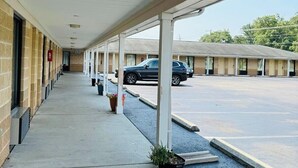 Un pasillo cubierto que conduce a un motel, con un estacionamiento visible al fondo.