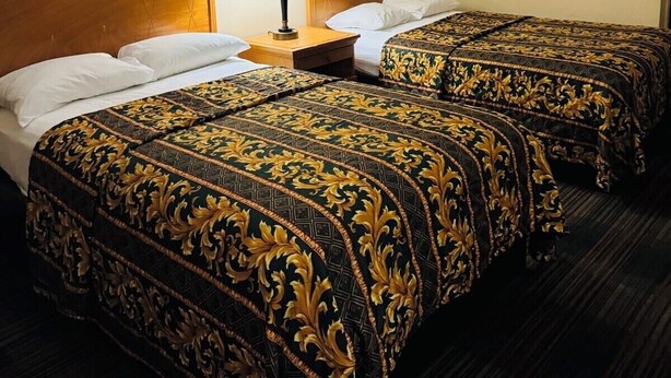 Una habitación de hotel con dos camas, cada una con cabecero de madera y una mesita de noche a juego con una lámpara.