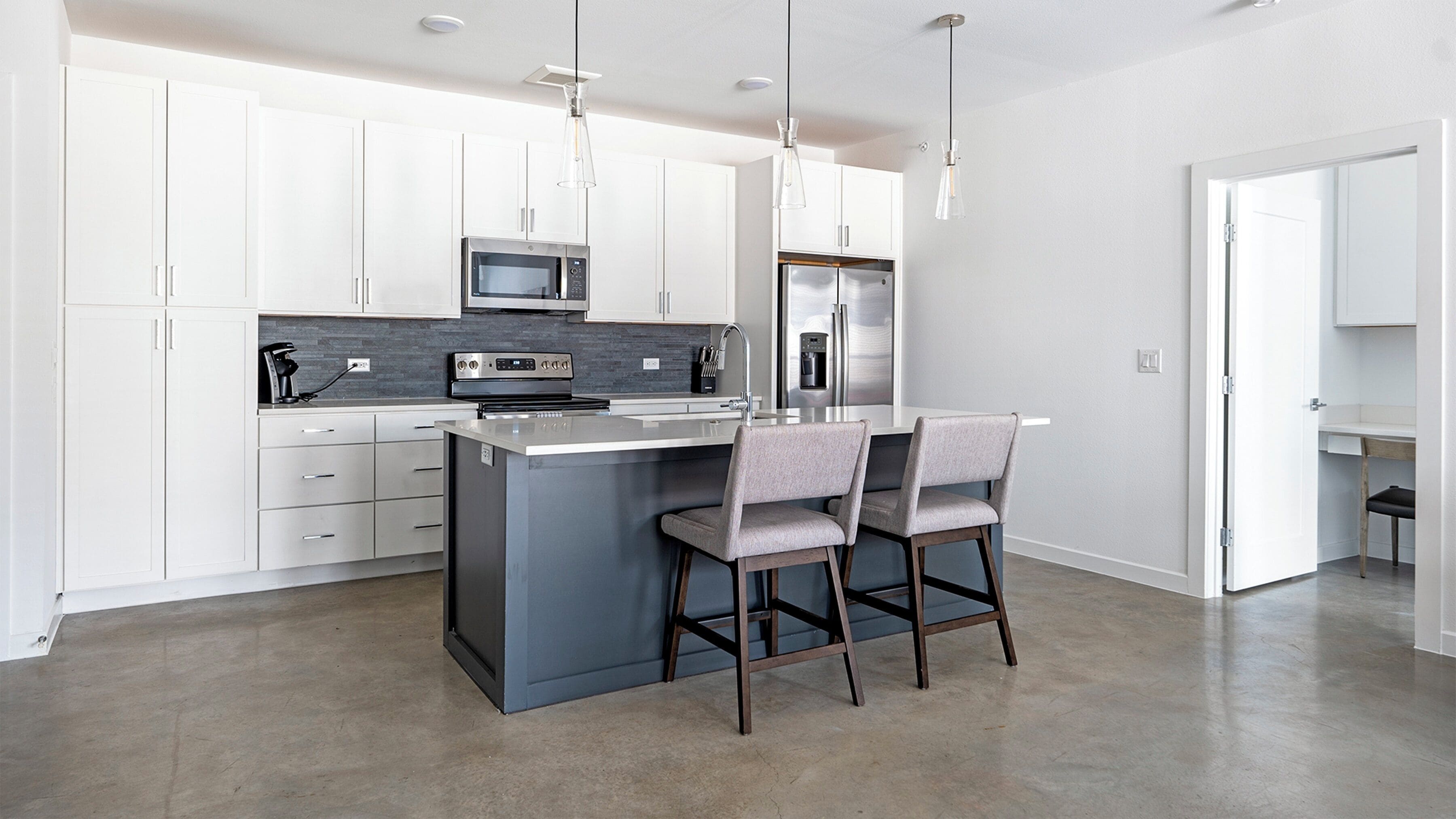 A modern kitchen with white cabinets, stainless steel appliances, and a central island with bar stools.