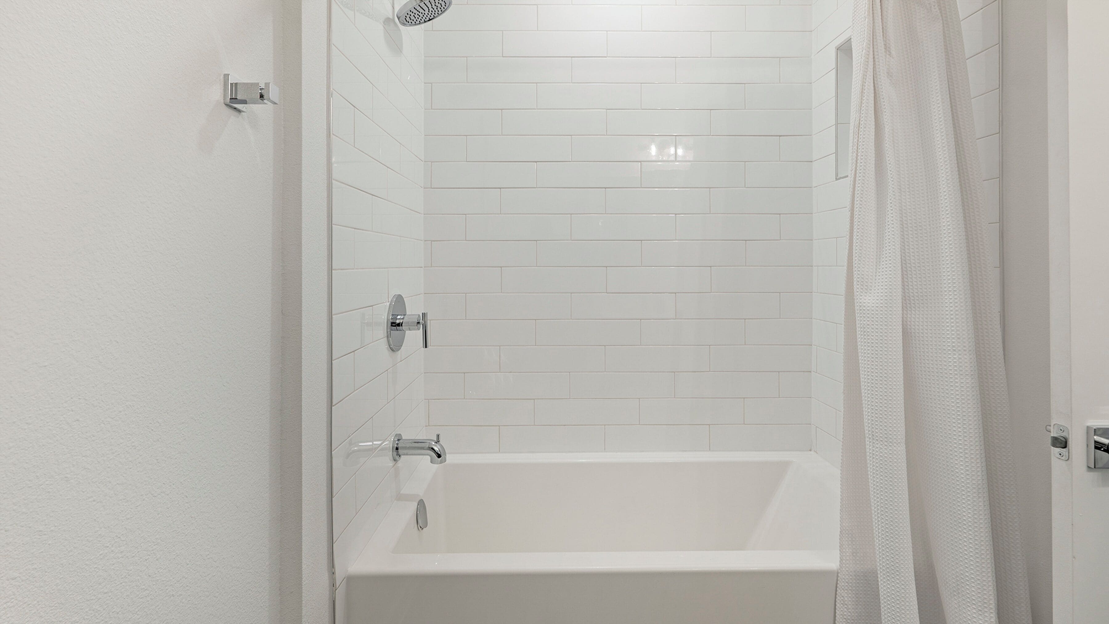 A modern bathroom with white tiles, a bathtub, and a shower area.
