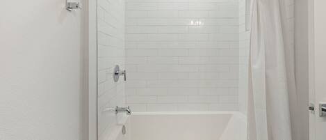 A modern bathroom with white tiles, a bathtub, and a shower area.