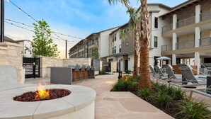 An outdoor patio with a fire pit, lounge chairs, and a pool area. - Hill Country Apartments by Landing (Spicewood)