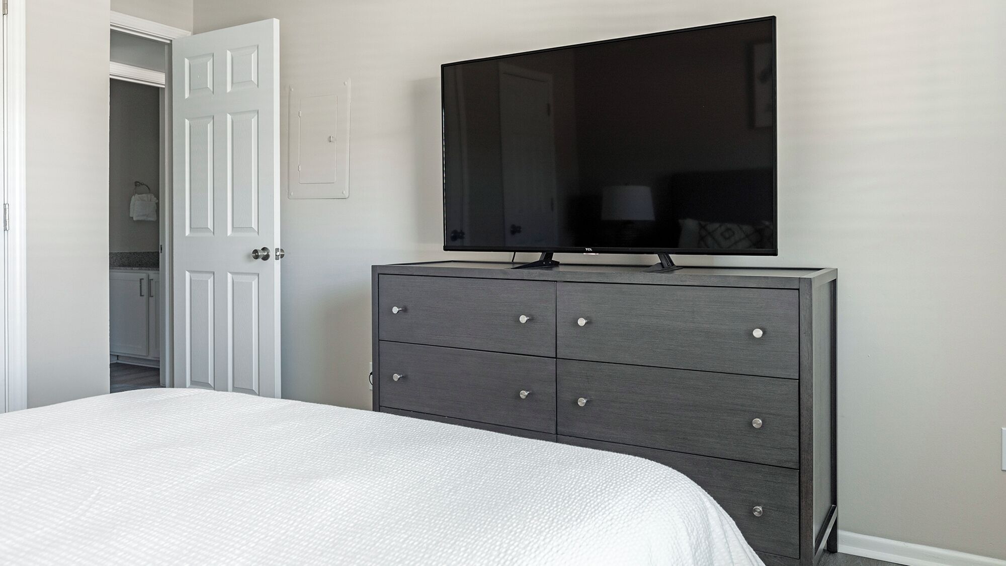 A bedroom with a bed, a dresser, and a TV mounted on the wall.