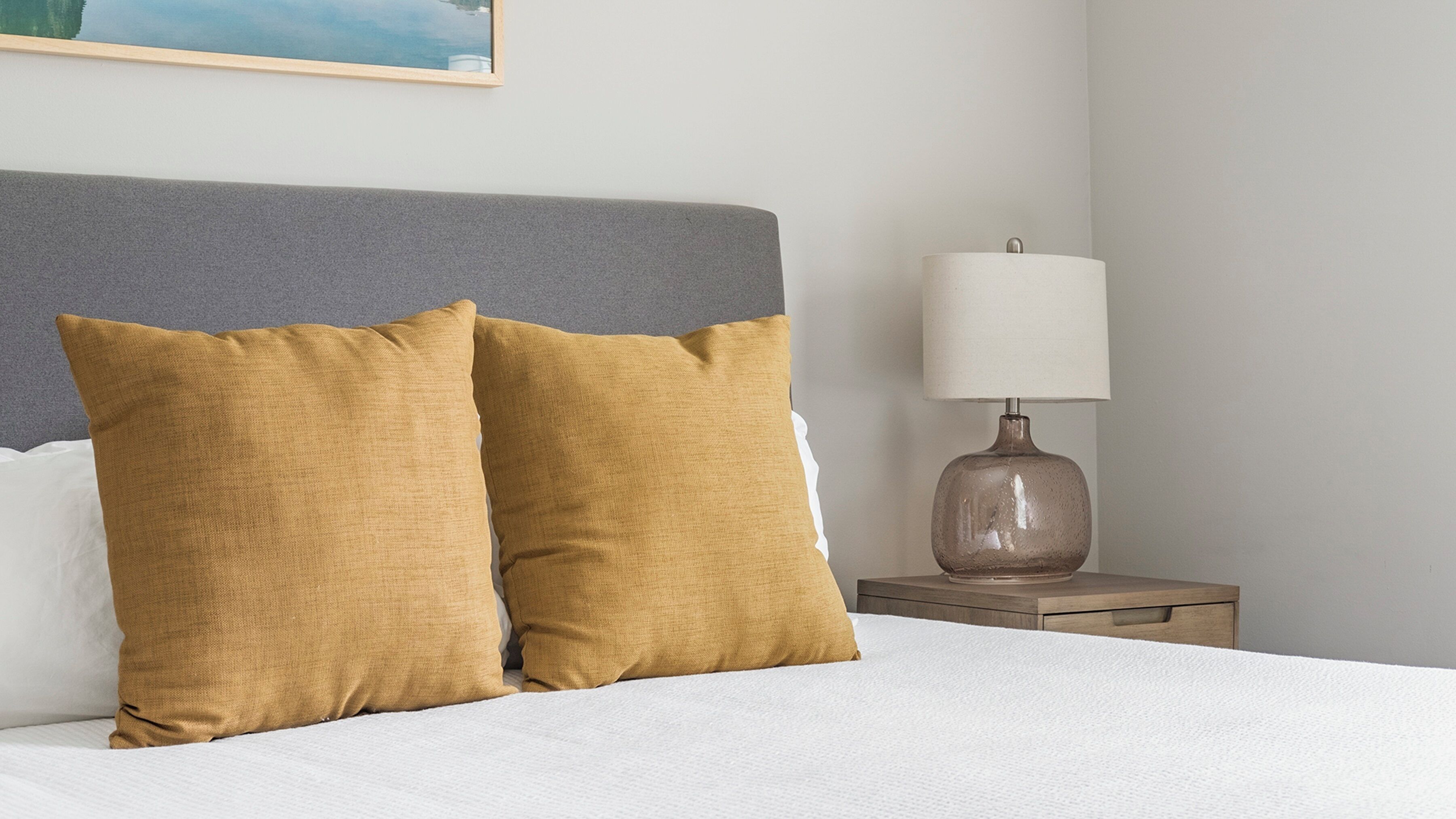 A neatly made bed with two pillows, a bedside lamp, and a gray headboard.