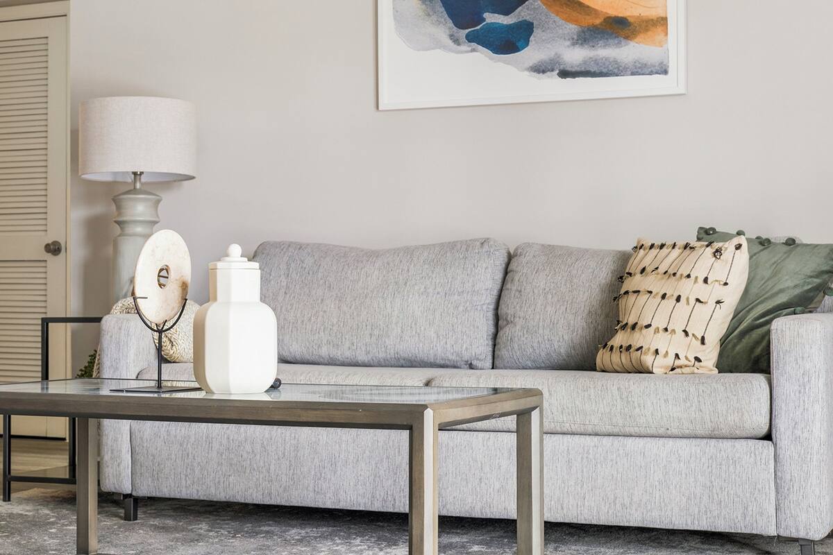 A living room with a grey sofa, a coffee table, a lamp, and a painting on the wall.
