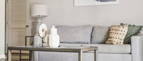 A living room with a grey sofa, a coffee table, a lamp, and a painting on the wall.