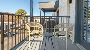 Un balcone con due poltrone in vimini e un tavolino, affacciato su un'area di parcheggio e edifici.