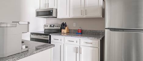 A modern kitchen with white cabinets, stainless steel appliances, a microwave, a stove, and a refrigerator.