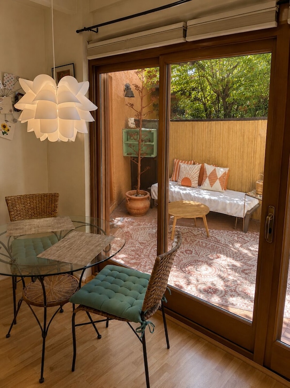 Une pièce avec une table en verre, des chaises, un canapé agrémenté de coussins à motifs, un luminaire suspendu et une vue sur l’extérieur.