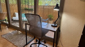 Ein Zimmer mit Schreibtisch, Stuhl und großen Fenstern mit Blick auf einen umzäunten Außenbereich.