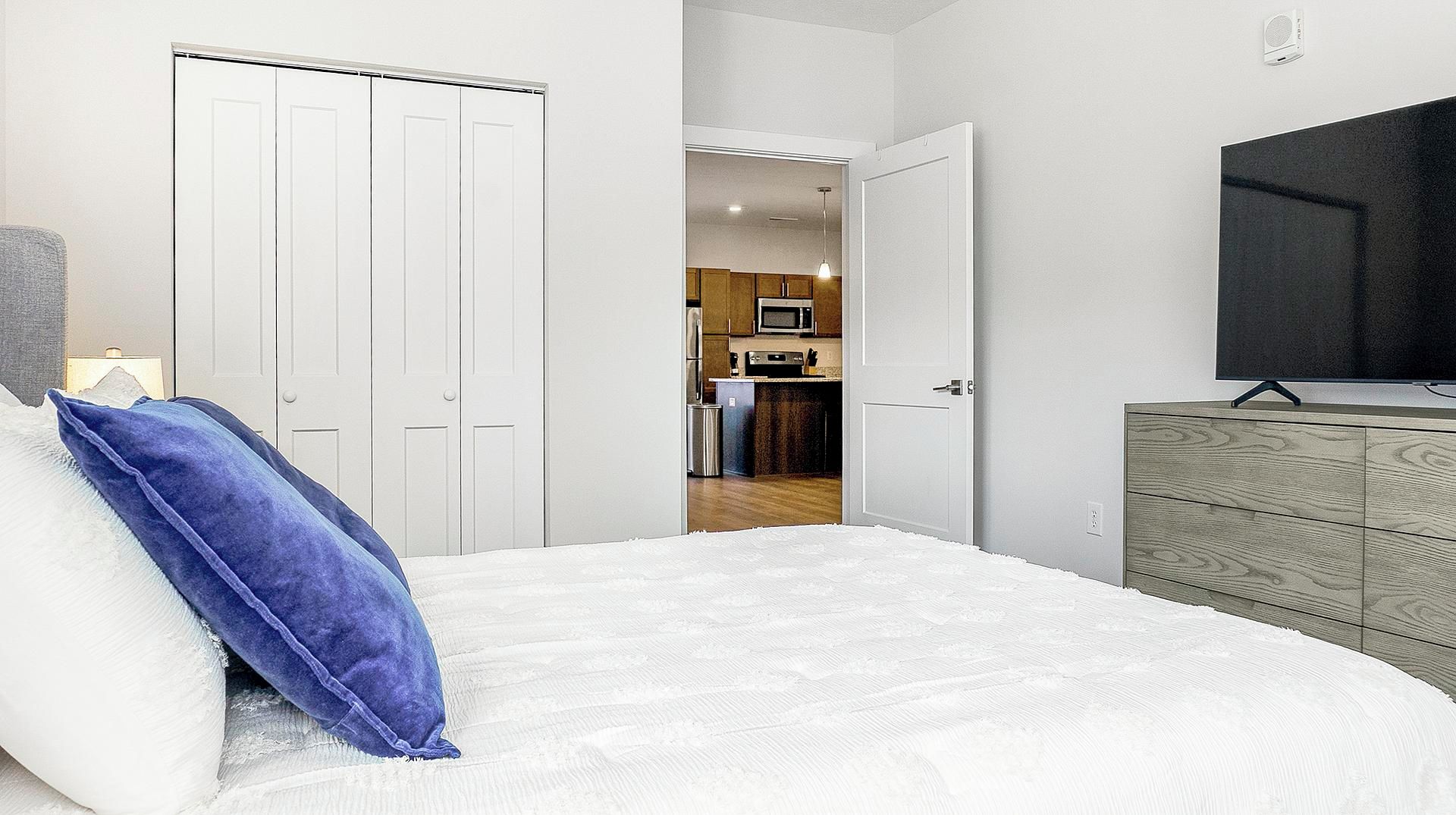 Una camera da letto con un letto, una cassettiera e una TV. Una porta dà accesso a una cucina.