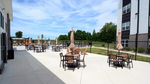 Eine Terrasse im Freien mit mehreren Tischen und Stühlen, umzäunt, mit einem Spielplatz im Hintergrund.