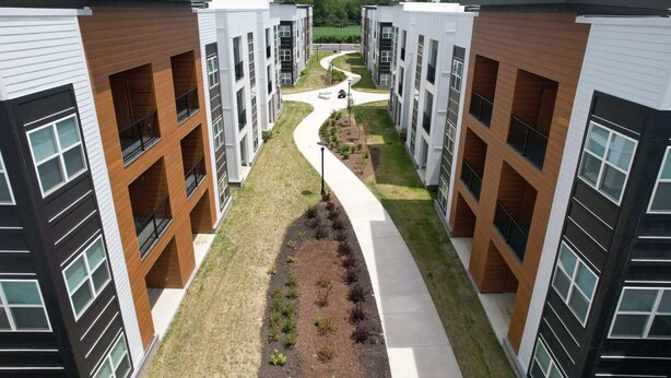 Ein modernes Apartmenthaus mit Innenhof, ausgestattet mit einem gewundenen Pfad und kleinen Bäumen.