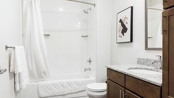 Un baño moderno con ducha envuelta en vidrio, inodoro blanco y lavabo sobre encimera de granito.