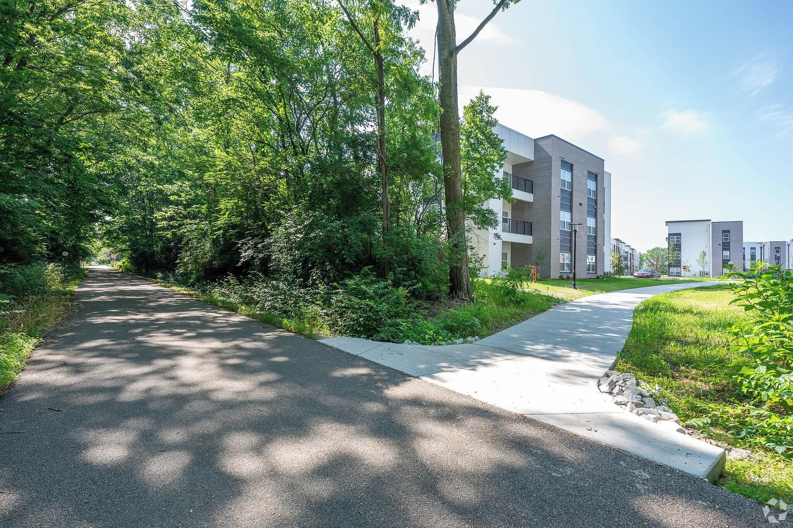 A pathway leading to a modern apartment building with a green landscape and trees.