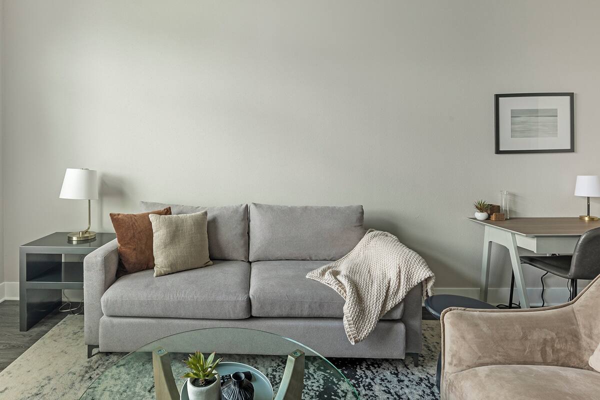 Un salon avec un canapé gris, deux tables d’appoint, une table basse en verre, un fauteuil et un tableau encadré accroché au mur.