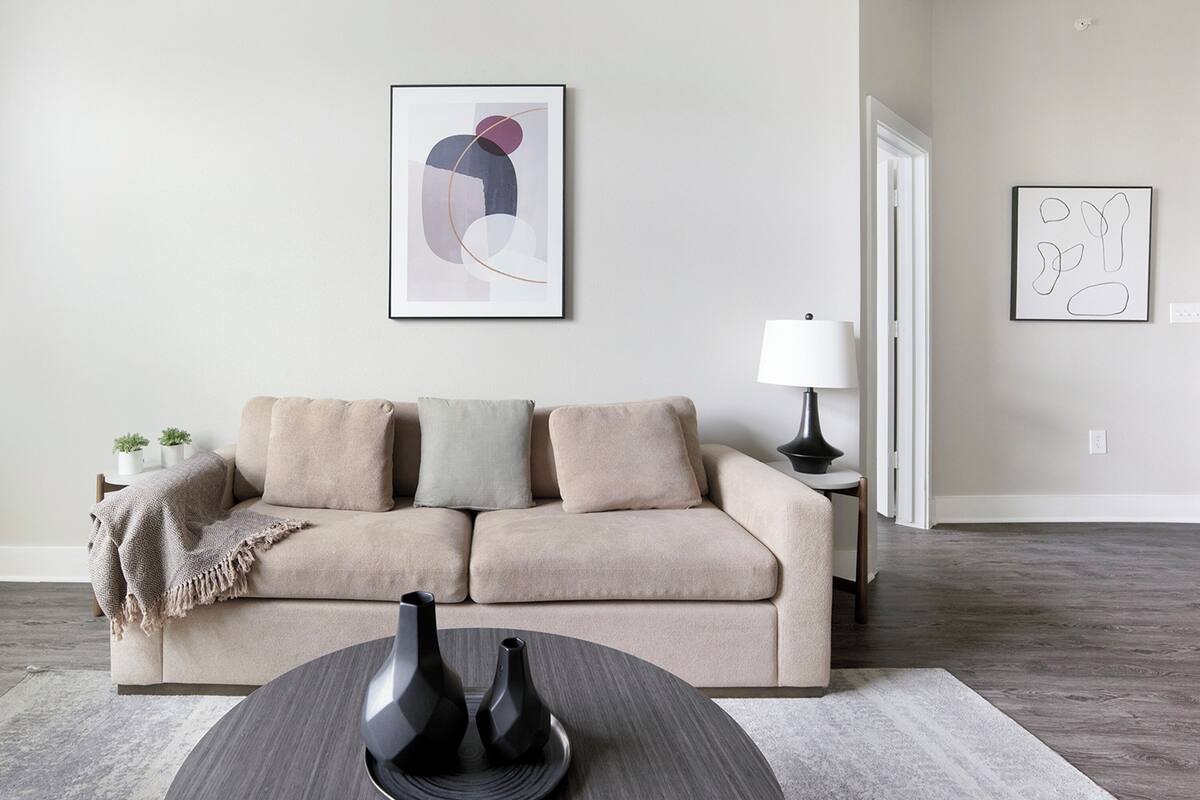 Un salon moderne avec un canapé beige, deux vases posés sur une table ronde et des œuvres d’art abstraites accrochées aux murs.