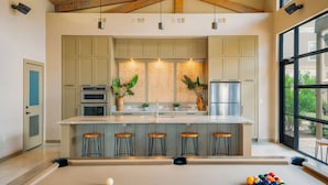 Una cocina moderna con una isla central, taburetes de bar y una mesa de billar.