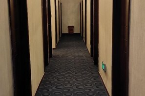 A hallway with a patterned carpet, wooden doors, and a trash bin. - 116 Business Hostel (Chongqing)