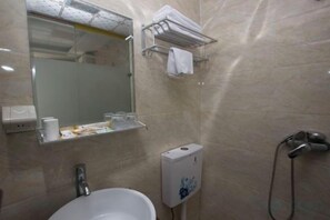 Un baño con lavamanos, espejo, toallero y secamanos.