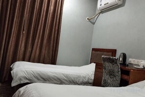 Habitación de hotel con dos camas individuales, una mesita de noche de madera, un hervidor y un enchufe.