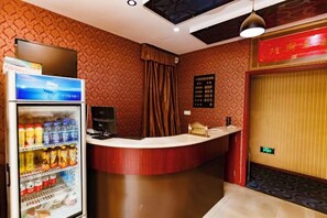 Un área de recepción con mostrador, un refrigerador lleno de bebidas y una pared con diseño decorativo.