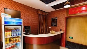 A hotel reception area with a counter, a refrigerator stocked with beverages, a television, and a decorative wall with a patterned design. - 116 Business Hostel (Chongqing)