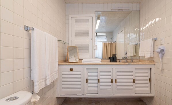 A bathroom with white tiled walls, a toilet, a sink with a mirror, and a hairdryer. - DAM Arquim20 (Mexico City)