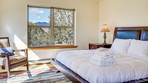 A bedroom with a large window, a bed with white bedding, a bedside table with a lamp, and a chair with a cushion. - Vacation Home With Breathtaking Views, Ample Parking and Pool Table (Cañon City)