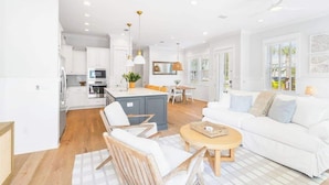 A modern kitchen with white cabinets, a central island, and a dining area with a white table and chairs. - 30A Seaside Escape by Stay on 30a (Inlet Beach)