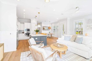 A modern kitchen with white cabinets, a central island, and a dining area with a white table and chairs.
