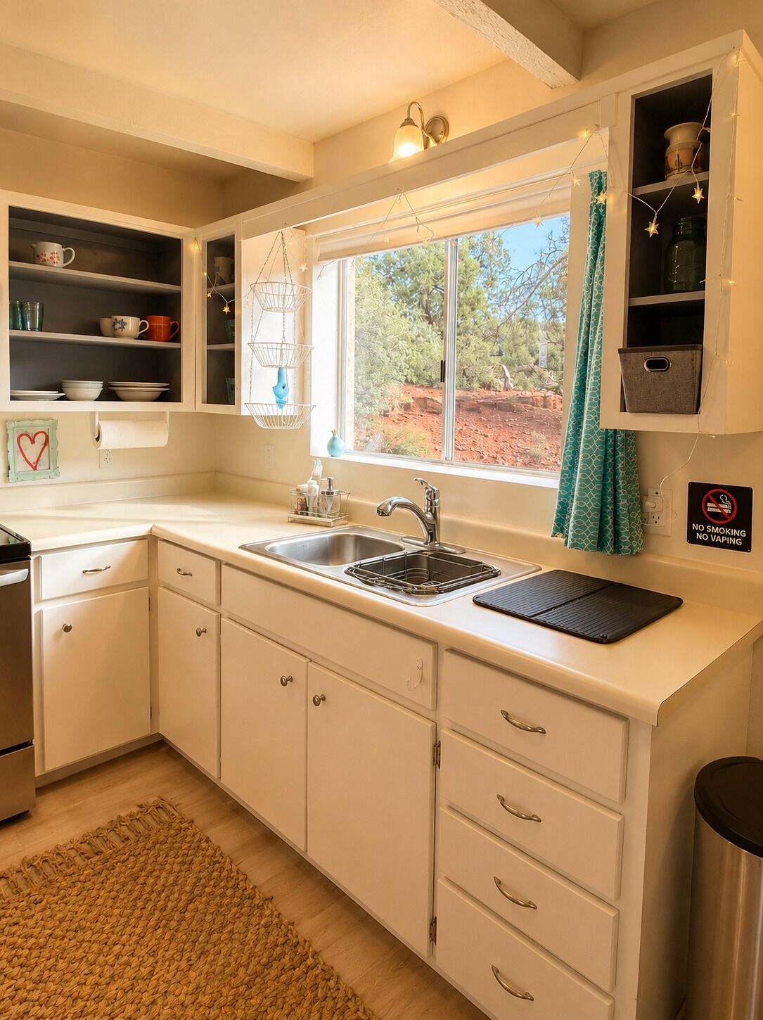 A kitchen with white cabinets, a stainless steel sink, a window with a view of trees, and a 'No Smoking' sign.