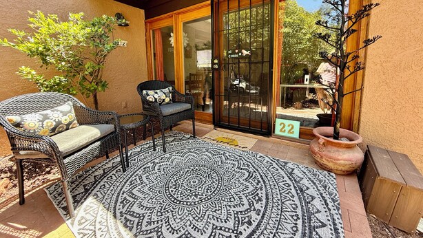 Un patio con mobiliario de mimbre, un tapete estampado y una planta en maceta.