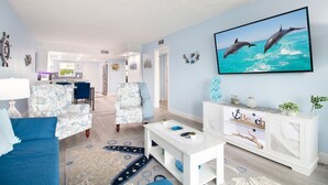 A living room with a blue couch, patterned armchairs, a white coffee table, and a TV displaying dolphins. - Intracoastal Waterways / Dolphin Sighting / YTC Resort (Indian Shores)