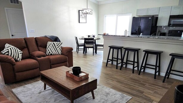 A living room with a brown sofa, a wooden coffee table, and a dining area with a round table and chairs. - Cupcake Mtn. View Tranquility (Lake Havasu City)