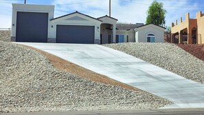 A residential area with two garage-style buildings, a paved driveway, and a landscaped hill. - Cupcake Mtn. View Tranquility (Lake Havasu City)