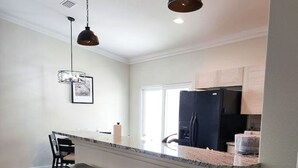 A modern kitchen with a central island, bar stools, pendant lighting, and a refrigerator. - Cupcake Mtn. View Tranquility (Lake Havasu City)