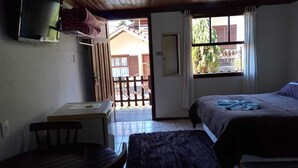 Een slaapkamer met een bed, een bureau, een televisie, een raam en een deur naar buiten.