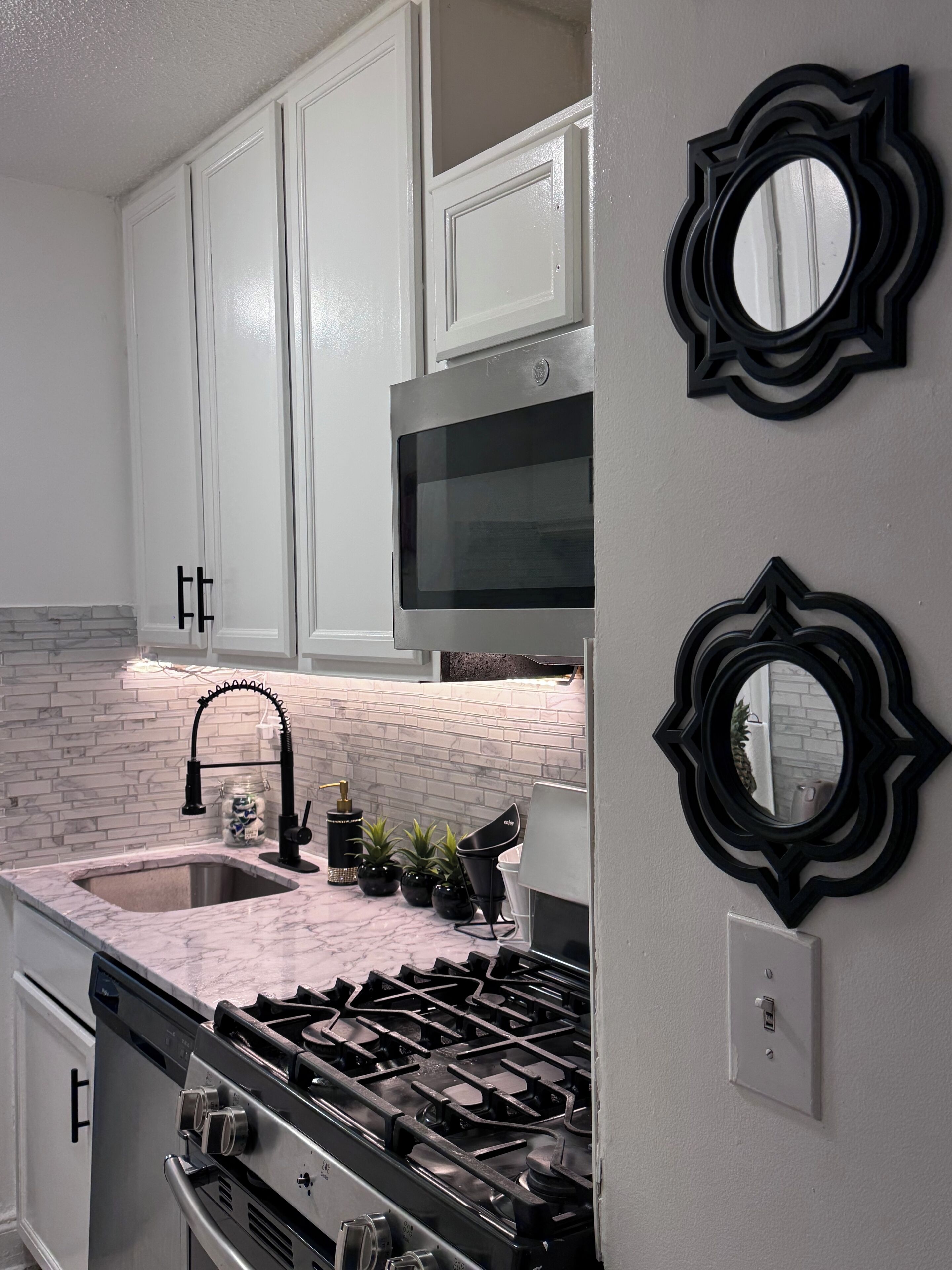 A kitchen with white cabinets, a stainless steel stove, a black faucet, and a microwave.