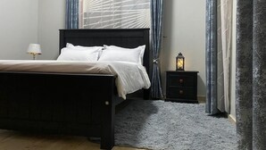 A bedroom with a bed, a nightstand, a lamp, and a window with curtains.