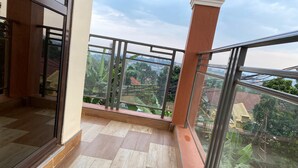 A balcony with a tiled floor, glass railings, and a view of greenery and buildings.