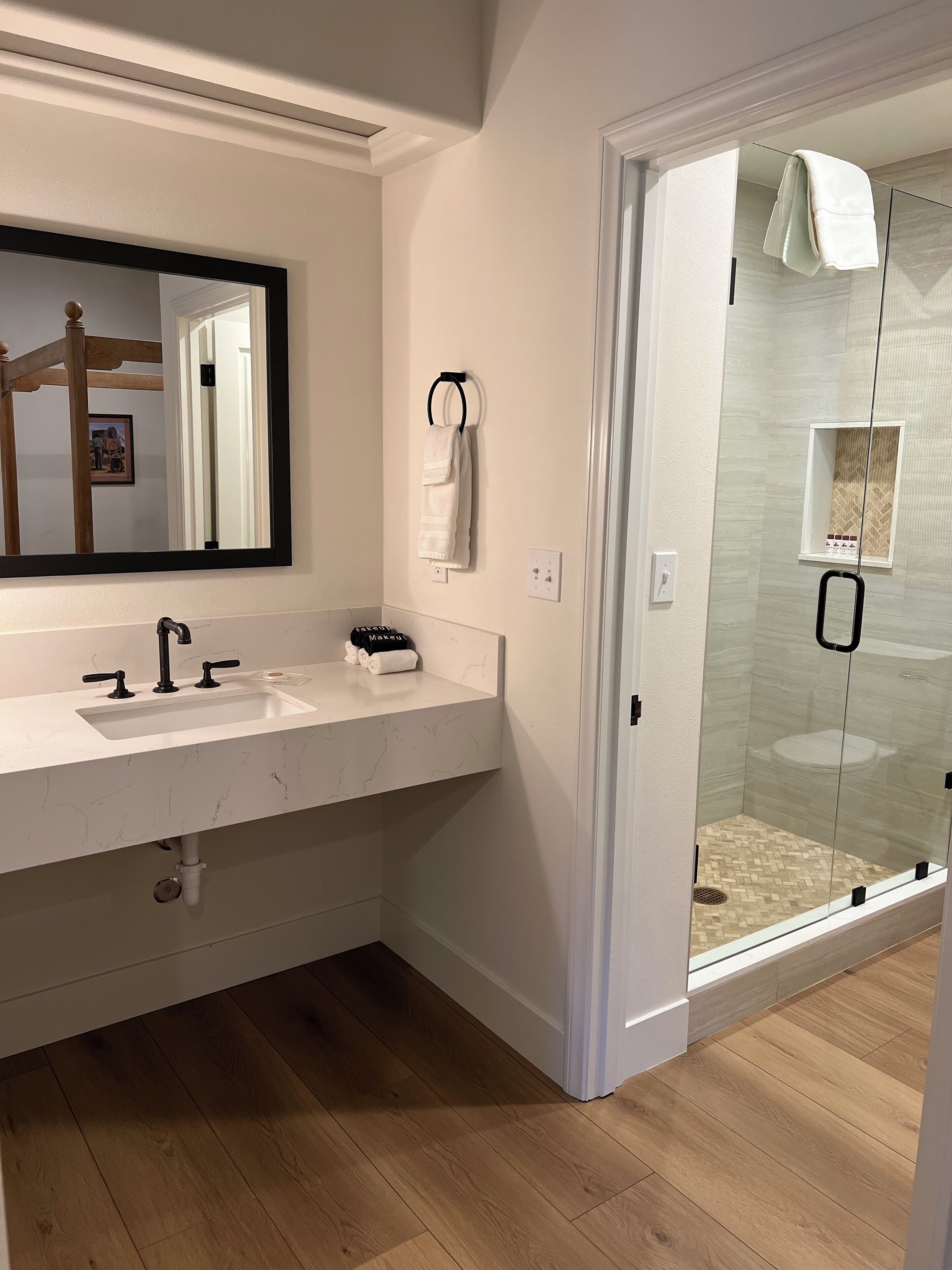 A modern bathroom with a white marble sink, a large mirror, and a glass-enclosed shower.