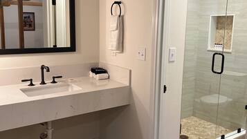 A modern bathroom with a white marble sink, a large mirror, and a glass-enclosed shower.