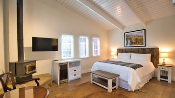 A bedroom with a bed, bedside tables, a TV, a fireplace, and a window with blinds.