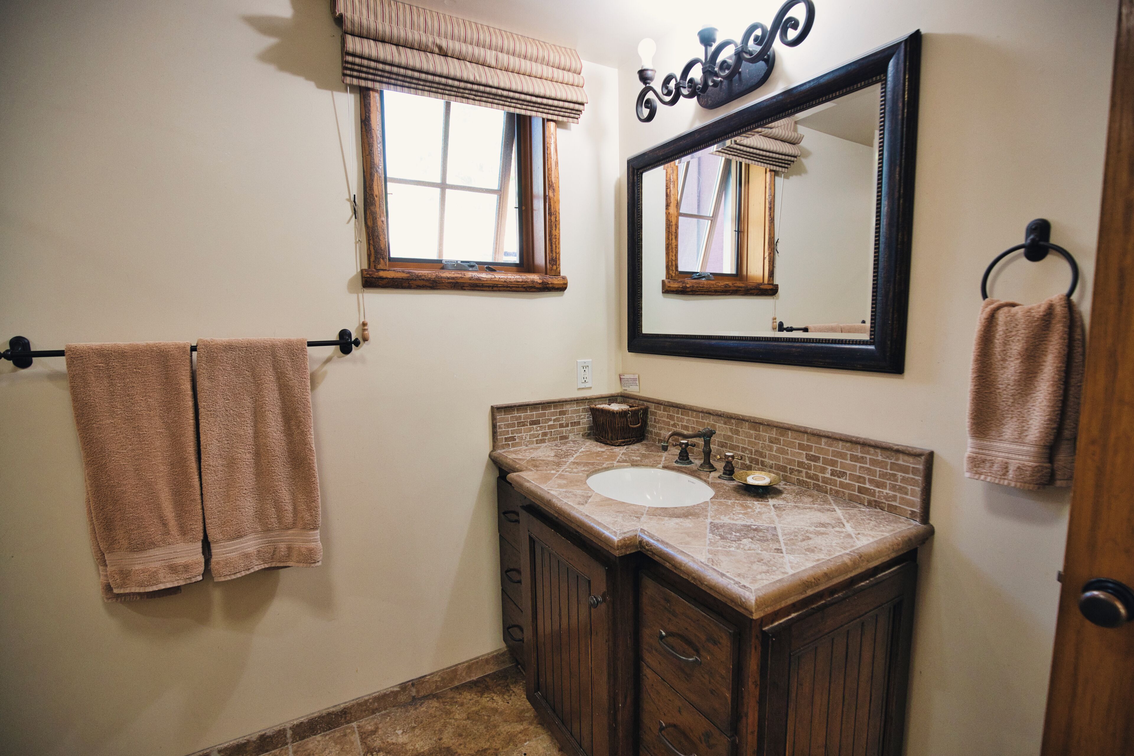 Un baño con lavamanos, espejo, toallero y ventana con persianas.