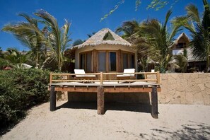Una estructura frente al mar con techo de paja, muelle de madera y dos sillones blancos.