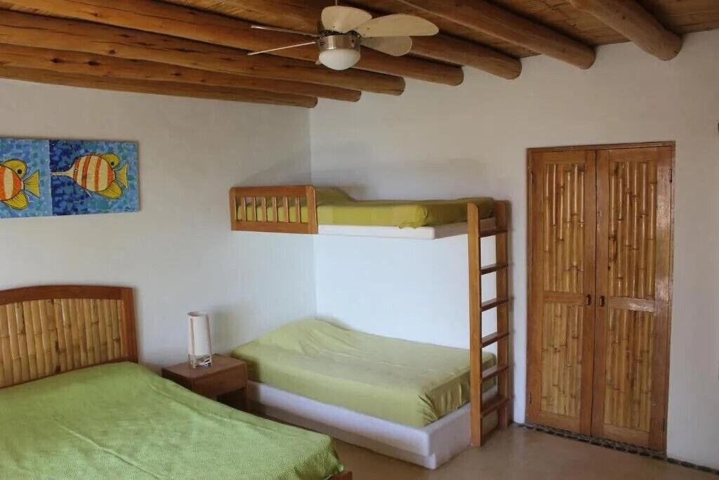 Habitación con literas, techo de madera, una cama individual con colcha verde, una mesita de noche, un cuadro de peces en la pared y un armario de madera.